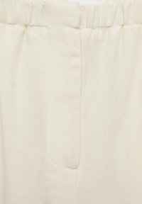 Crèmekleurige broek met een elastische tailleband, met zijzakken en een gladde, zachte stoftextuur. Eenvoudige stiksel-details zichtbaar.