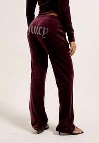 Bordeaux velours trainingsbroek met een losse pasvorm, voorzien van strassletters die "Juicy" aan de achterkant spellen. Soepele textuur, elastische tailleband.