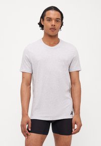 T-shirt gris à manches courtes avec un col rond. Tissu doux et léger avec une texture subtile. Présente un accent logo noir près de l'ourlet.