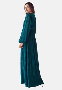 Türkises Langarmkleid aus strukturiertem Stoff mit vertikalen Falten, das einen lockeren Schnitt und eine fließende Silhouette aufweist, entworfen für Komfort.