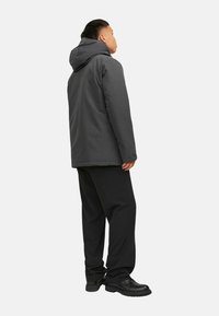 Grey hooded jacket with a smooth texture, paired with loose black pants and sturdy black shoes. The jacket has a simple, functional design.