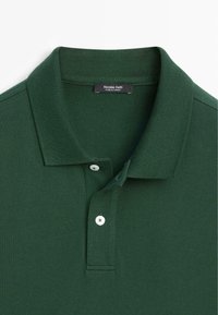 Polo à manches courtes vert foncé avec col côtelé, deux boutons blancs et étiquette de marque "Massimo Dutti" cousue à l'intérieur du col.