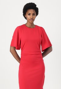 Abito rosso realizzato in un tessuto morbido ed elasticizzato. Presenta maniche corte a palloncino, scollo rotondo e arricciature in vita per un silhouette aderente.