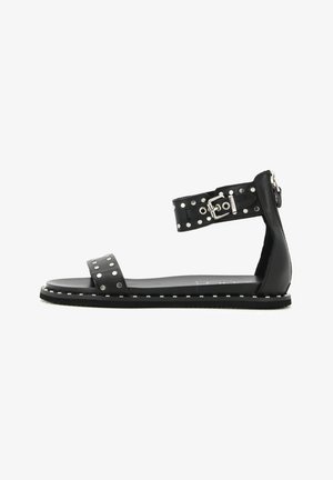 Sandal in pelle nera con suola piatta, dettagli borchiati sulla cinghia e chiusura a fibbia con zip laterale per una vestibilità sicura.