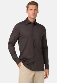 Hnědá dlouhá košile s límečkem a předními knoflíky. Hladká textura a slim fit design. Nosit s světle béžovými kalhotami.