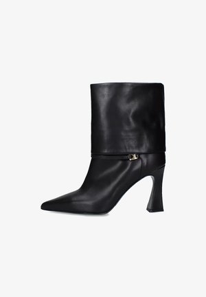 Stivale alto in pelle nera con tacco alto, punta affilata, design a metà polpaccio e parte superiore piegata, con un accento dorato alla caviglia.
