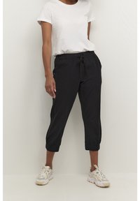 Zwarte cropped broeken met elastische tailleband en trekkoord, voorzien van zijzakken en manchetten. Gepaard met een witte T-shirt en sneakers.