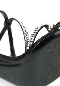 Sandale noire à talon haut avec des fines lanières ornées de petits strass transparents et une semelle texturée visible depuis un angle inférieur.