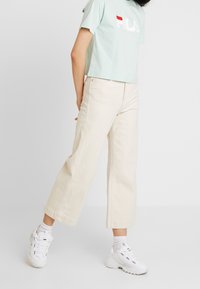 Camiseta corta de color azul claro con el logo "Fila" en rojo y blanco, combinada con pantalones anchos de color blanco roto y zapatillas blancas.