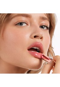 Auftragen von Lippenstift in einem zarten Rosa mit einem metallischen roségoldenen Röhrchen. Glatte Textur auf den Lippen und natürlicher Hautfinish, der die Gesichtszüge betont.