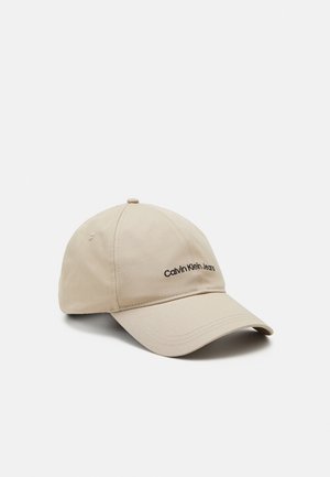 Beżowa czapka baseballowa z zakrzywionym daszkiem i czarnym haftowanym logo "Calvin Klein Jeans" na przednim panelu.