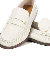 White leather loafers with stitched detailing and a decorative hardware accent. Rounded toe and flexible brown rubber sole.