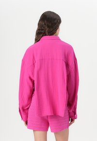 Camicia rosa over-size sgualcita con polsini con bottoni e dettaglio della cucitura posteriore, abbinata a pantaloni corti rosa testurizzati.
