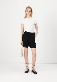 White fitted short-sleeve top paired with black shorts featuring scalloped hem, black lace-up flats, and a small white handbag.