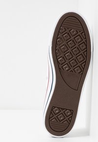 Semelle d'une chaussure blanche Converse All Star montrant une semelle en caoutchouc marron avec des motifs géométriques et un détail du logo de la marque.