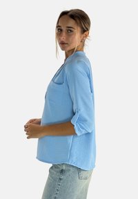 Hellblaues Langarmhemd mit aufrollbaren Manschetten und Brusttasche. Hergestellt aus strukturiertem Stoff, verfügt es über eine lockere Passform und einen abgerundeten Saum.