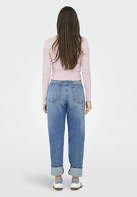 Lyserød langærmet top med flæser forneden, parret med højtaljede, løst fit blå denim jeans, oprevet i manchetterne, og hvide sneakers.