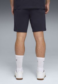Shorts en coton bleu marine, longueur mi-cuisse, avec un design simple et un ourlet cousu. Portés avec des chaussettes blanches et des baskets.