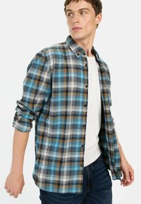 Blauwe, bruine en witte geruite flanellen shirt met knoopsluiting, opgerolde mouwen en een zachte textuur, gedragen over een wit T-shirt.
