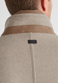 Beige Wollmischjacke mit einem braunen Wildlederkragen. Verfügt über eine gestickte Naht und ein schwarzes Etikett mit "MILESTONE" in der Nähe des Kragens.