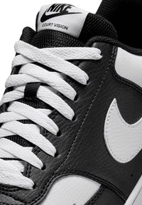 Sneaker in pelle nera con dettagli bianchi e superficie texture. Presenta lacci bianchi e un'etichetta nera sulla linguetta con la scritta "Nike Court Vision."