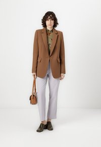 Hnědý šitý blazer, zelená květinová blůza, světle levandulové kalhoty, hnědá crossbody taška a tmavé boty se lesklým povrchem.