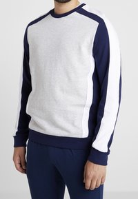 Felpa grigia e blu navy con strisce laterali bianche, colletto e polsini a coste, texture morbida, caratterizzata da una vestibilità rilassata e senza loghi visibili.