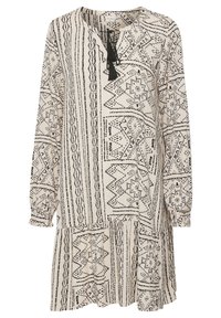 Långärmad, löspassad klänning i ljusbeige med svarta geometriska mönster. Anmärkningsvärda egenskaper inkluderar en v-ringning med ett knyt och en flerlagers fåll.