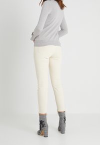 Jasnoszary dopasowany sweter, kremowe obcisłe dżinsy z postrzępionymi brzegami oraz szare kraciaste botki za kostkę z czarną kwiatową haftowaną dekoracją.