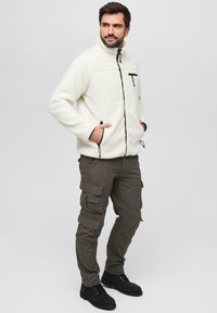 Kreemvalge fliisjakk mustade tõmblukkude ja taskute aktsentidega. Kanda oli oliiviroheline cargo-pants, millel on mitu taskut ja lõdvestatud lõige.
