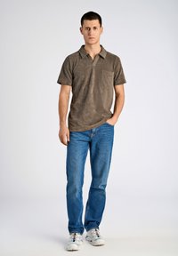 Brun polotröja med korta ärmar och ficka, i kombination med blå jeans och vita sneakers. Enkel, avslappnad design och texturerad tyg.