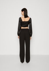 Crni kratki crop top s nabranešom i napuhanih rukavima, u kombinaciji s crnim hlačama visokog struka. Glatka tekstura i minimalistički stil.
