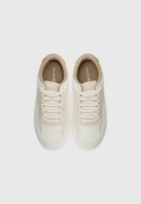 Sneakers bianchi e beige con tomaia in pelle liscia e tessuto, punta tonda, suola bianca spessa e lacci piatti. Nome del marchio visibile all'interno.