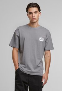Gray cotton t-shirt with a round neckline and short sleeves, featuring a white graphic logo on the left chest.