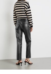 Zwarte leren broek met een gladde textuur, rechte pasvorm en achterzakken, gecombineerd met een gestreepte zwart en beige trui. Sandalen met dunne bandjes.