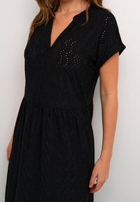 Vestido corto negro de manga corta con escote en V, que presenta un patrón de ojales, tejido texturizado y cintura fruncida.