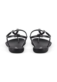 Black sandals featuring a flat sole, thin adjustable straps, and a textured footbed with a decorative loop detail at the front.