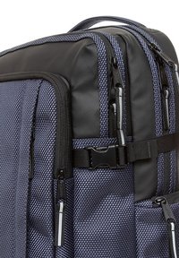 Mochila en azul marino con tejido texturizado, acentos negros, múltiples cremalleras y una correa con hebilla. Cuenta con asas acolchadas y correas ajustables.