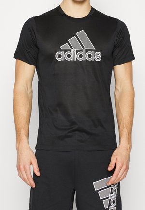 Man draagt een zwarte Adidas T-shirt en bijpassende zwarte short met zichtbare Adidas-logo's op beide kledingstukken.