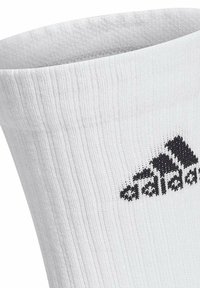 Calcetín atlético blanco con textura acanalada, con un logo negro de Adidas en el lateral. La parte superior tiene un puño reforzado para mayor soporte.