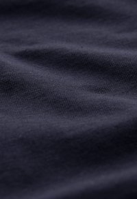 Gros plan sur un tissu bleu foncé avec une texture fine en maille visible et de légers plis à la surface.