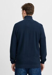 Tengerészkék kötött pulóver magas gallérral, texturált anyaggal, bordás mandzsettával és alsó szegéllyel. Akadálytalan hátrésze van, látható rögzítők nélkül.