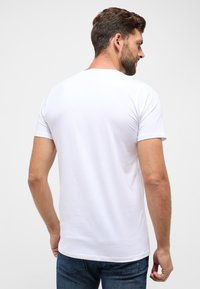 Hvid kortærmet t-shirt lavet af bomuld, med rund hals og en glat tekstur. Set fra ryggen, parret med blå denimjeans.