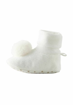 Biele pletené ponožky s preklopeným lemom, s huňatou pom-pom ozdobou a bodkovanou protišmykovou podrážkou.