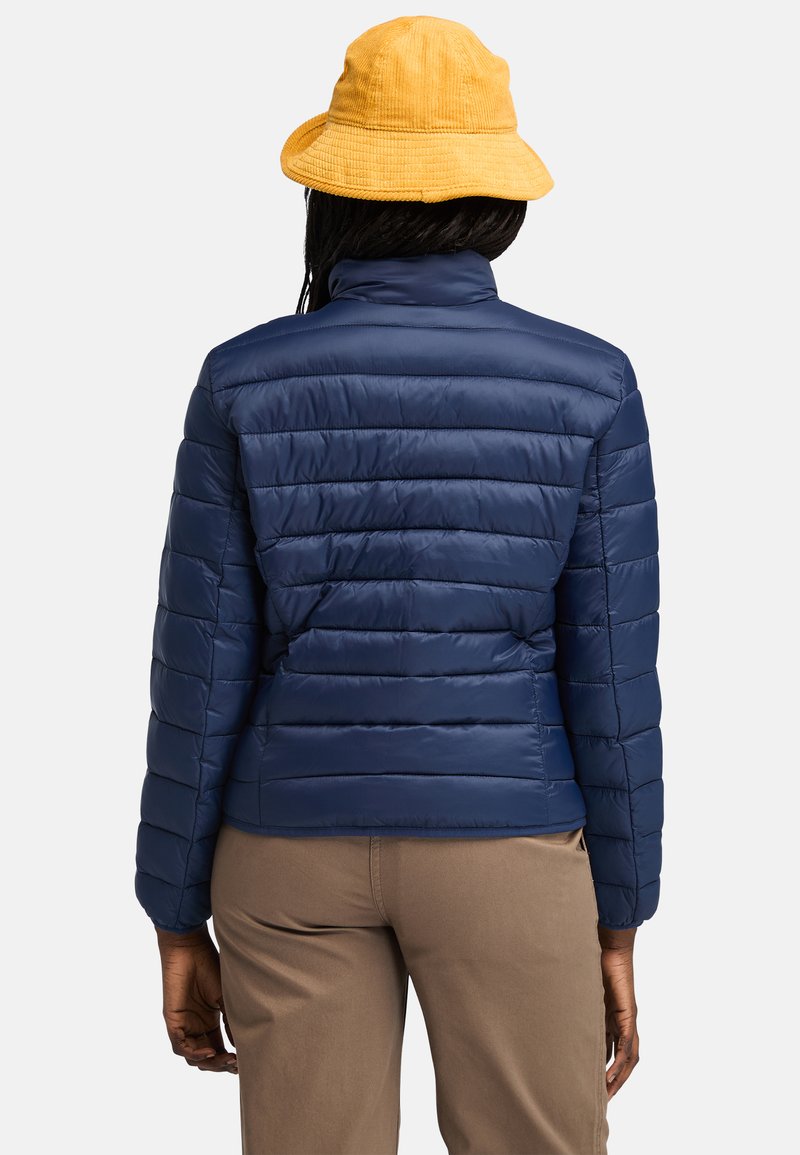 Giacca imbottita blu navy con imbottitura a righe orizzontali, colletto alto e vestibilità slim. Indossata con un cappello a secchiello in corduroy giallo.