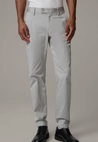 Ljust grå byxor med sidfickor och subtil textur, figursydda vid midjan, tillsammans med svarta skor. Designen är skräddarsydd för en åtsittande passform.