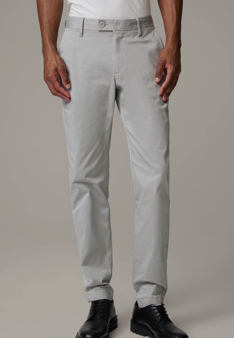 Ljust grå byxor med sidfickor och subtil textur, figursydda vid midjan, tillsammans med svarta skor. Designen är skräddarsydd för en åtsittande passform.