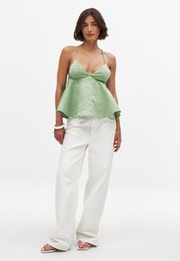 Roheline satiinist kampsik, millel on kortsutatud tekstuur ja laienev äär, koos valgete laiade pükstega ja lihtsate sandaalidega.