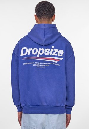 Modrý flísový svetr s velkým bílým logem "Dropsize" na zadní straně, doplněný červenými a modrými akcentními liniemi a žebrovanými manžetami a lemem.