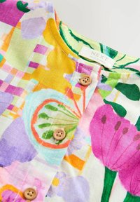Colorful floral shirt collar with wooden buttons and a label reading "NEXT Made in India" on a white background.